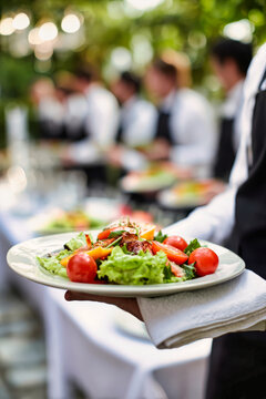 A waiter in a white shirt and black apron holds a plate of salad