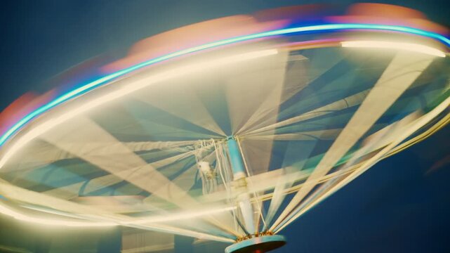 Empty chain swing ride lit with bright LED lights during evening twilight. Fairground atmosphere, recreation, leisure and carnival attraction theme. 4K.