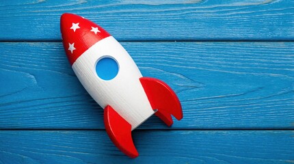 Fototapeta premium Colorful wooden toy rocket on blue wood background. Red, white spaceship model with star decor for kids. Creative childhood play concept about space travel, adventure, cosmic exploration. Fun object