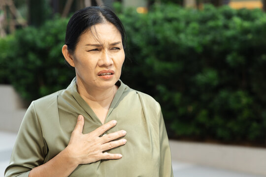 Southeast Asian woman panting with hand on chest in outdoor park, concept image for shortness of breath, GERD, asthma