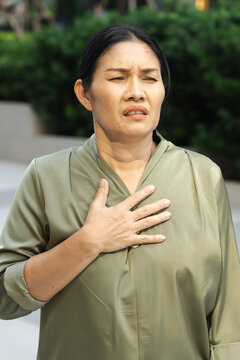 Southeast Asian woman panting with hand on chest in outdoor park, concept image for shortness of breath, GERD, asthma