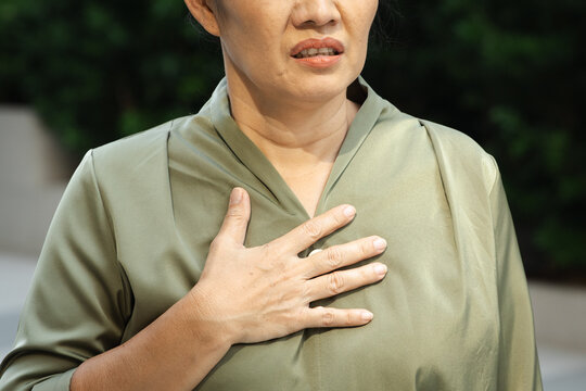 Southeast Asian woman panting with hand on chest in outdoor park, concept image for shortness of breath, GERD, asthma, hand closeup shot