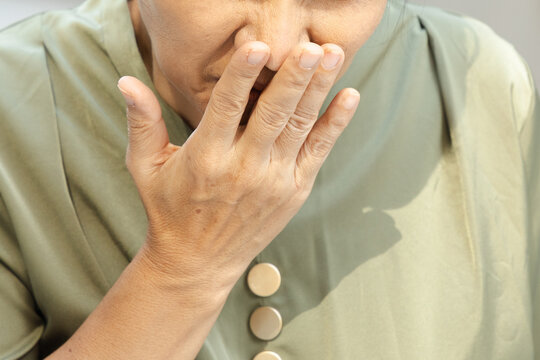 50s Southeast Asian woman gagging and nauseous in a park, covering her mouth with grimace expression, hand closeup shot