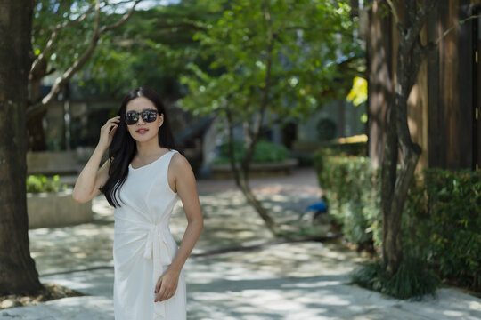Woman posing in white dress and sunglasses, enjoying an outdoor park lifestyle