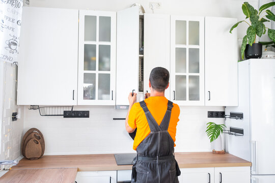 Back view of a male professional assembler adjusting white kitchen overhead glass cabinets, furniture assembly, professional service.