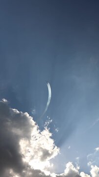 Vertical screen Aerobatic jets climb steeply in tight formation leaving long white smoke trails across a vast blue sky above sunlit clouds during an impressive aerial display show