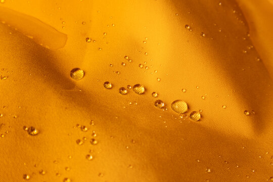 Macro shot of raindrops on vibrant orange hydrophobic fabric surface close-up