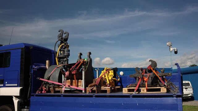Heavy hydraulic attachments and industrial lifting equipment secured with straps on a blue flatbed truck for safe transportation of machinery parts used in construction and rescue