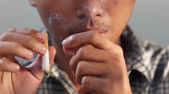 Close up of an unhealthy young Asian man is coughing and exhaling smoke when smoking cigarette.