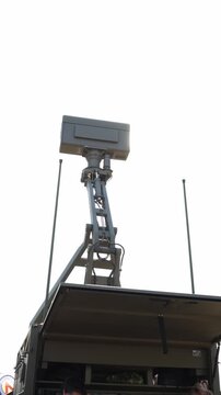 Vertical screen Military radar antenna mounted on an elevated mobile platform for airspace surveillance and aircraft detection with bright sunlight shining behind the radar unit