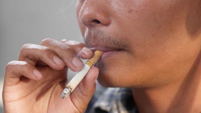 Close up of a young Asian man is smoking cigarette.