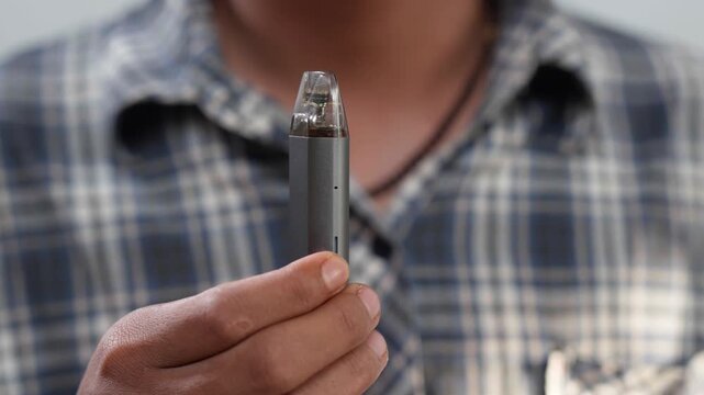 Close up of an Asian man holding a vape device or electric cigarette.