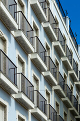 Building facade featuring a repeating pattern of balconies with black railings and patterned undersides, set against a vibrant blue sky in Cadiz, Spain © photoopus