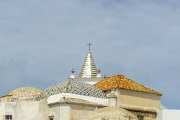 Ornate church domes and a colorful bell tower steeple with a cross rising above the rooftops, showcasing traditional Andalusian architecture in Cádiz, Spain © photoopus