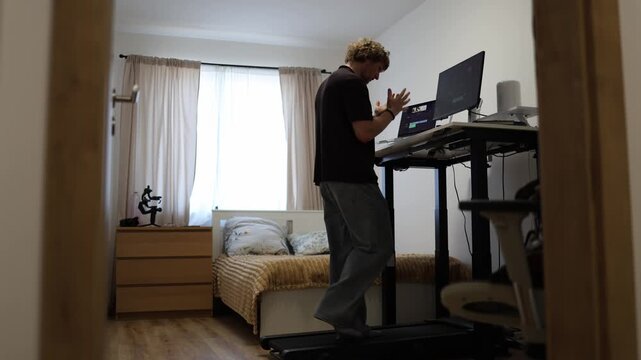 Frustrated video editor struggles with poor quality footage while working on his computer and walking on a treadmill at home realizing the recorded material may be unusable