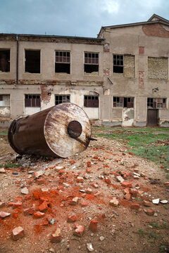 Rusty overturned metal tank on a pile of red bricks in front of a dilapidated factory building with broken windows, Moynaq, Uzbekistan