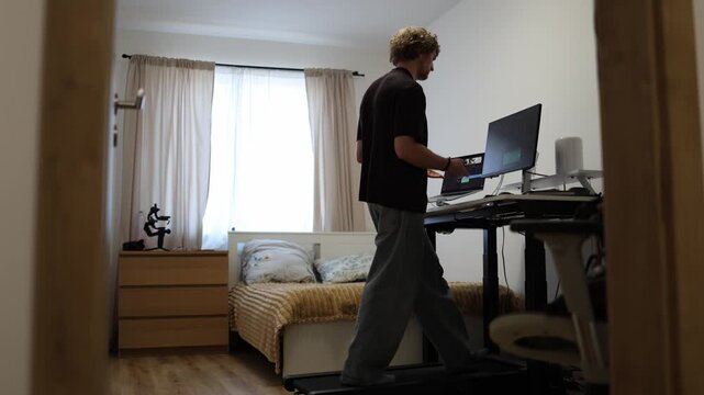 Electric standing desk automatically rises to a comfortable working height as a young man starts his remote workday at home preparing his computer workspace for daily office tasks