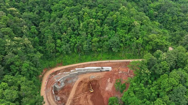 An ongoing road reconstruction after severe rainfall triggered slope failure, showcasing excavators, reinforced retaining structures, and engineering efforts to prevent future landslides. Thailand.
