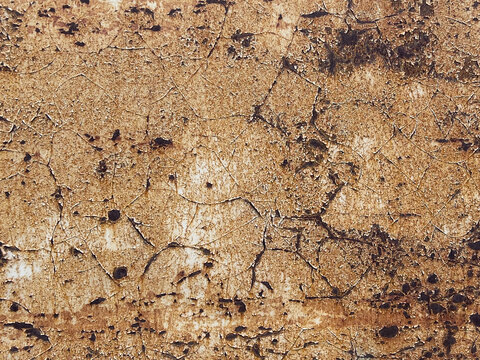 Closeup of cracked peeling paint and rust texture on weathered wall surface with warm brown and beige tones