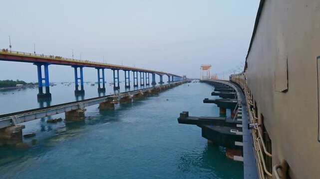 POV video from a moving train crossing Pamban Railway Bridge near Rameswaram, Tamil Nadu, India, showcasing the railway tracks, turquoise seawater, and parallel bridge structure along the coast.