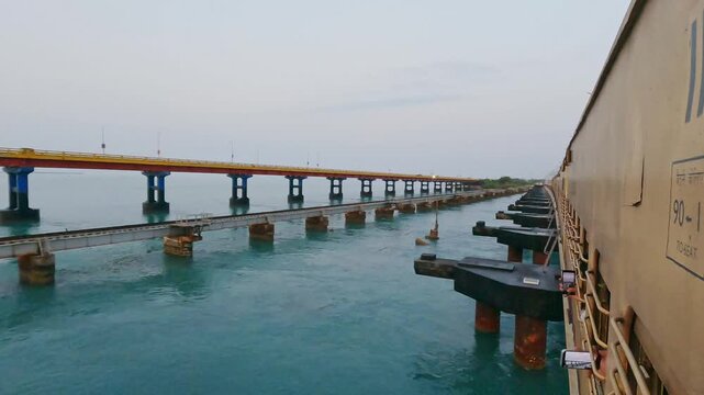 POV video from a moving train crossing Pamban Railway Bridge near Rameswaram, Tamil Nadu, India, showcasing the railway tracks, turquoise seawater, and parallel bridge structure along the coast.