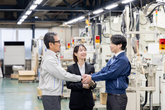 工場で握手する作業員グループ。事業承継、M&A、協力、チームワーク、仲介、紹介、コンサル、笑顔、契約