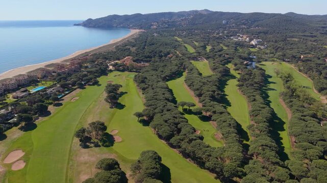 Breathtaking aerial footage capturing the stunning landscape of a lush golf course situated next to a sandy beach and the serene mediterranean sea on a beautiful sunny day in pals, girona