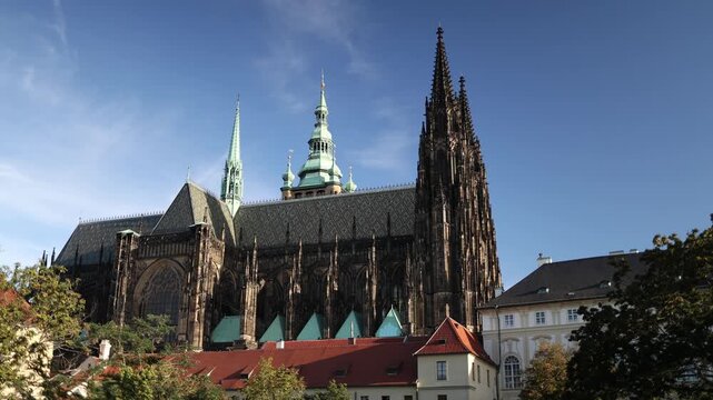 Smooth panoramic camera movement captures a wide view of St Vitus Cathedral at Prague Castle with Gothic towers detailed stone architecture and historic rooftops under blue skies