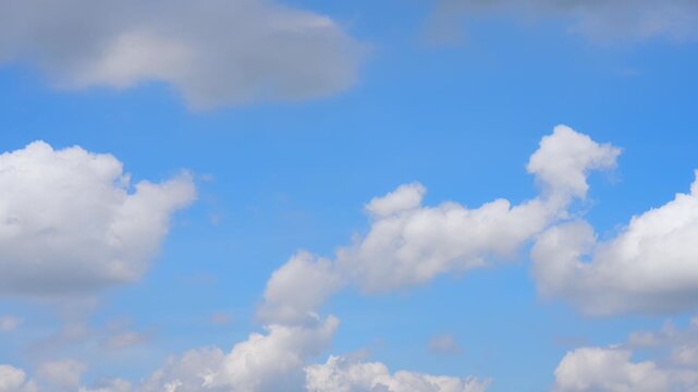 A blue sky timelapse video captures scattered cumulus clouds with soft white edges and gray undersides, drifting and changing shape as gentle winds create dynamic cloud patterns in the daylight sky.
