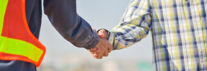 Close-up of Two Professionals Shaking Hands in Construction Area, Signifying Partnership and Trust in Industrial Collaboration, Outdoors on a Bright Day © Suriyo