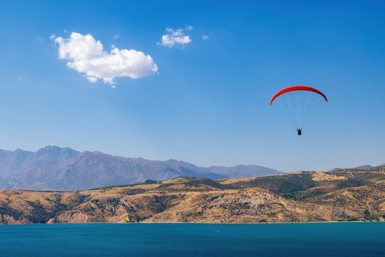 A paraglider soaring above Lake Charvak, a popular destination for summer sports in the Tian Shan mountains, Uzbekistan 