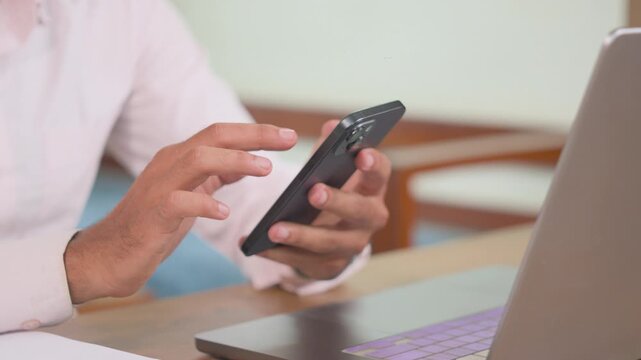 Close-up of a young professional using a phone while working beside a laptop at home. Suitable for mobile business, digital communication, remote work, multitasking and professional lifestyle.