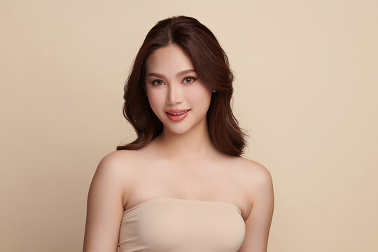 A beautiful young Asian woman with clean, fresh skin against a beige background. Skincare, facial treatment, cosmetology, beauty, and spa. An elegant portrait of an Asian woman.