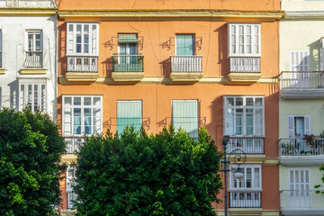 Ornate balconies and windows adorn the vibrant orange and white building facades, capturing the unique architecture and urban charm of a sunny street in Cádiz © photoopus