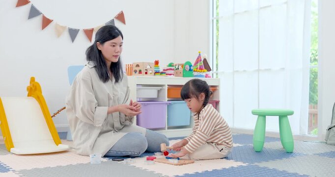 Asian single mother coaches preschool daughter in educational floor play at home, encouraging shape matching with wooden blocks and gentle hand motion, supporting child development, patience, bonding.