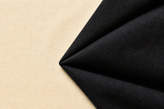 A close-up of a beige fabric meeting a black fabric at a sharp corner.