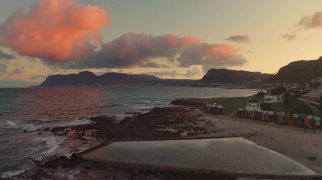 Breathtaking coastal landscape featuring pink sunset clouds above the ocean with mountains in the background and a calm tidal pool near the shore