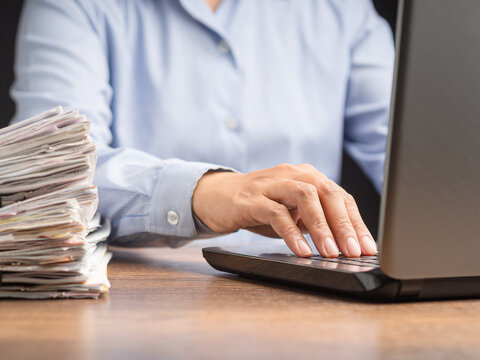 Employee working on laptop beside stack of documents  