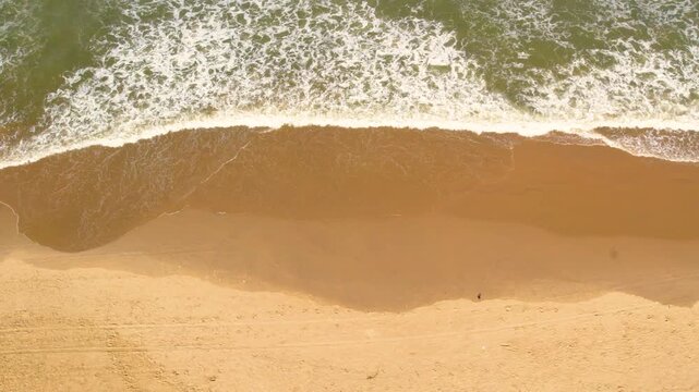 Aerial drone view of waves crashing on the golden sand of vagator