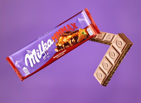 Milka Mmmax Mandel Karamell almond and caramel milk chocolate packaging with floating chocolate pieces on a purple background, featuring exposed filling and selective focus.