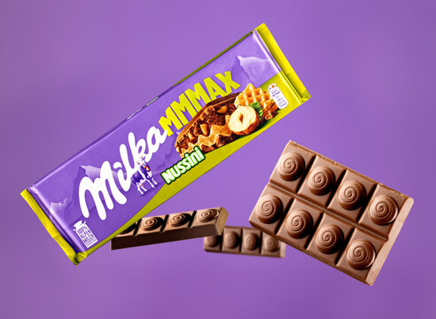 Milka Mmmax Nussini hazelnut and wafer milk chocolate packaging with three floating chocolate pieces on a purple background, combining a detailed foreground piece with softly blurred background pieces