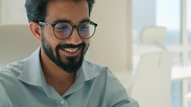 Happy Indian Arabian male business man smiling typing laptop in office working computer remote job glad muslim executive manager businessman networking program project online startup indoor workplace