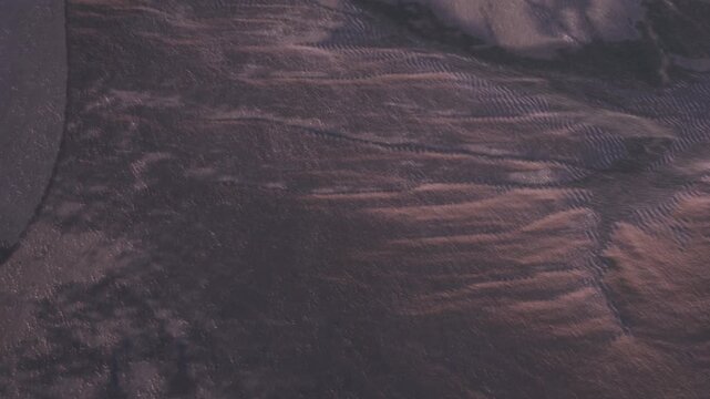 A stunning view captures the intricate textures and unique patterns of sand along the shoreline. The sun begins to set, illuminating the serene waters and leaving a tranquil atmosphere.