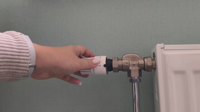 Adjusting the radiator temperature a hand wearing a watch adjusts the thermostatic valve. Heating season, turning on the heat, cold time of year.