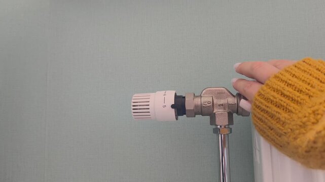 Adjusting the radiator temperature a hand in a yellow sweater adjusts the thermostatic valve. Heating season, turning on the heat, cold time of year