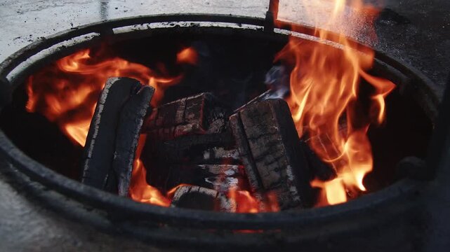 Close shot of an open fire burning beneath a cooking griddle, with bright orange flames rising from the fire pit and wood burning intensely below the hot plate.