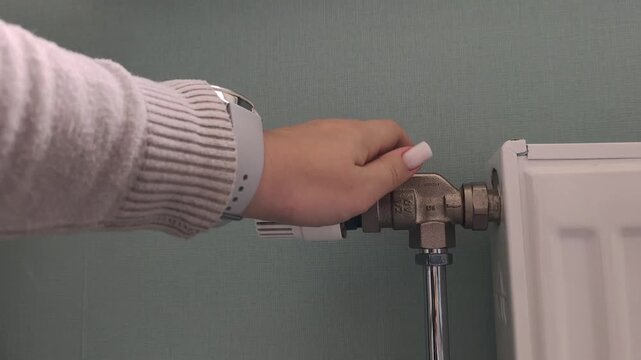 Adjusting the radiator temperature a hand wearing a watch adjusts the thermostatic valve. Heating season, turning on the heat, cold time of year.