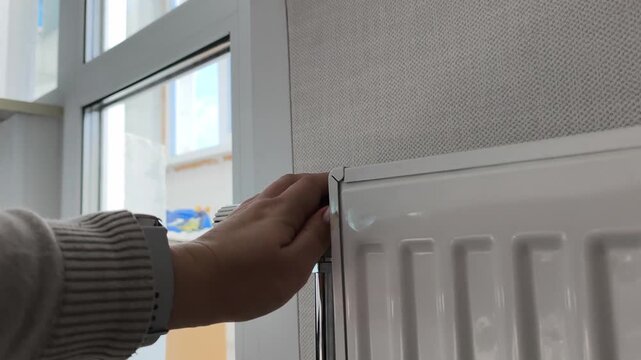 Adjusting the radiator temperature a hand wearing a watch adjusts the thermostatic valve. Heating season, turning on the heat, cold time of year.