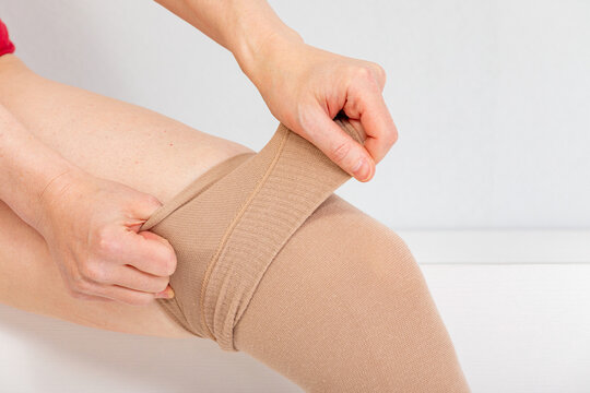 Person pulling on beige compression stockings over leg. Medical hosiery for circulation support and everyday wear. Compression therapy and leg care. Healthcare, wellness and self-care