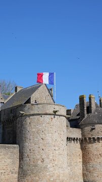 French flag waving above historic Mont Saint Michel abbey walls in strong coastal wind, symbolizing France heritage, national identity and cultural tradition
